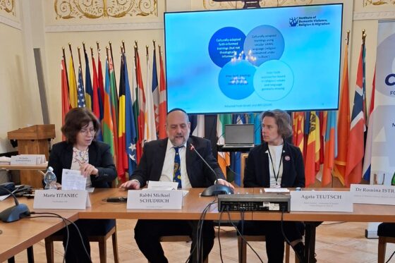 zdjęcie przedstawia rabina i dwie kobiety siedzących przy stole i okmawiających zagadnienie